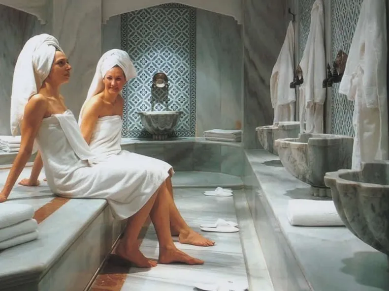 Two guests in towels resting beside marble basins